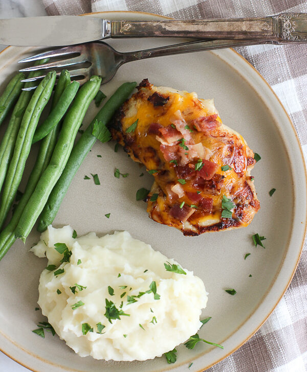 Cheddar cheese ranch chicken thighs with bacon served on a plate with mashed potatoes and green beans