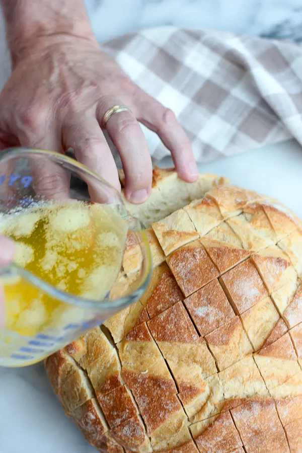pouring the garlic butter into the slices of the cheesy bloomin' crusty Italian bread
