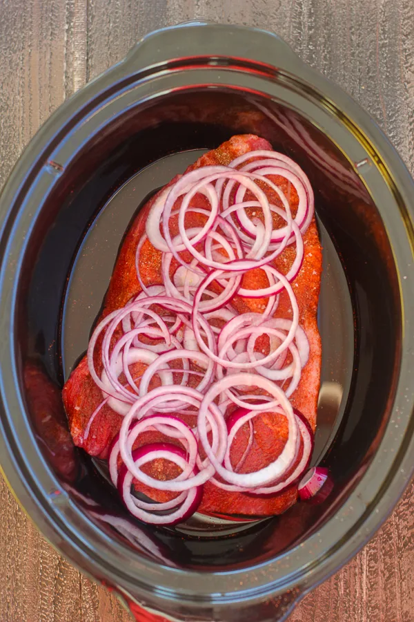 Seasoned Brisket topped with sliced onions in the slow cooker before cooking