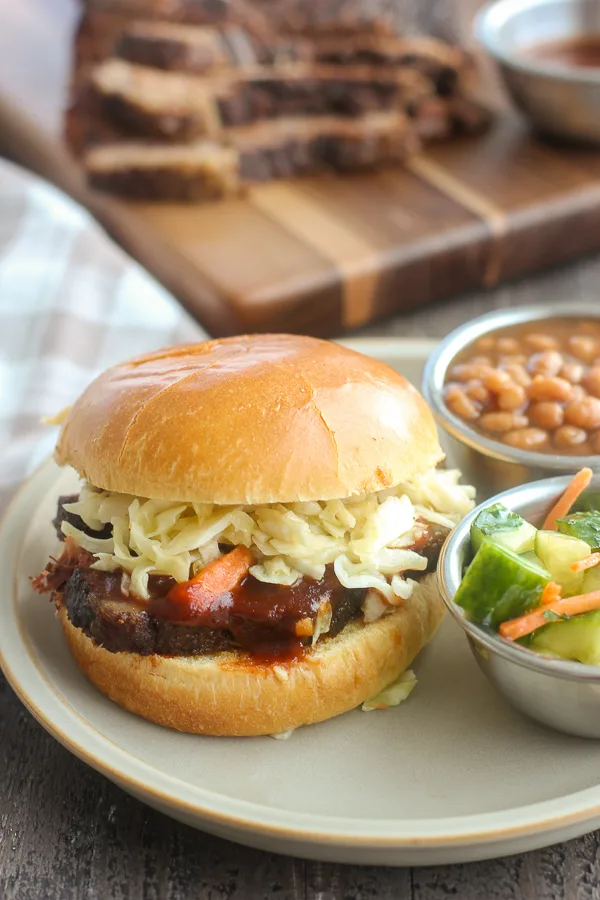 Close up photo of Slow Cooker Barbecue Brisket Slider plated with baked beans and cucumber salad