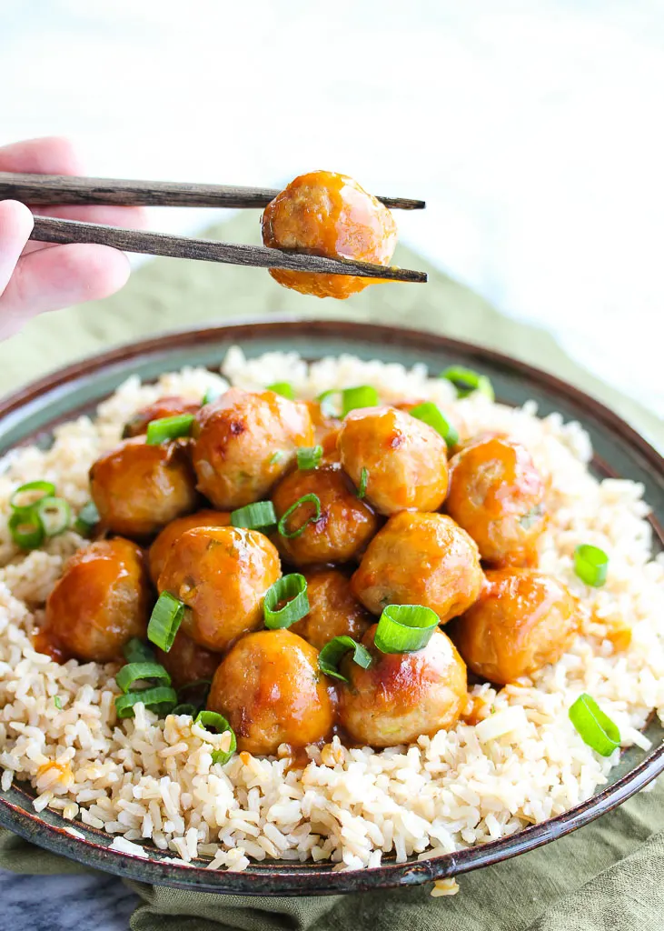 Plate of orange meatballs over rice. Holding one meatball with chop sticks