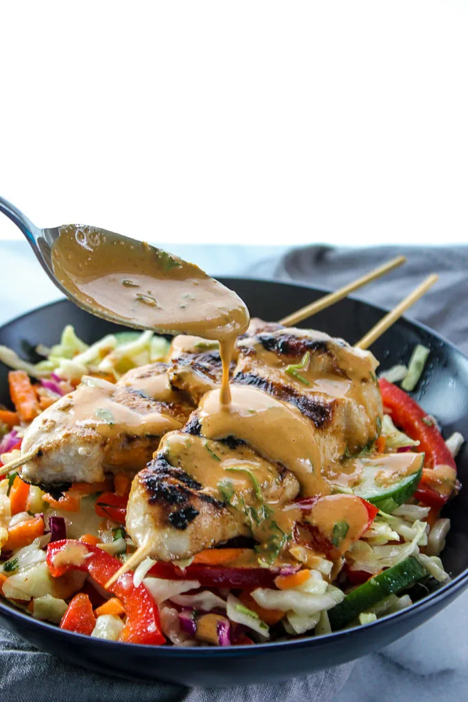 Drizzling peanut sauce over the grilled chicken skewers on top of the Asian slaw