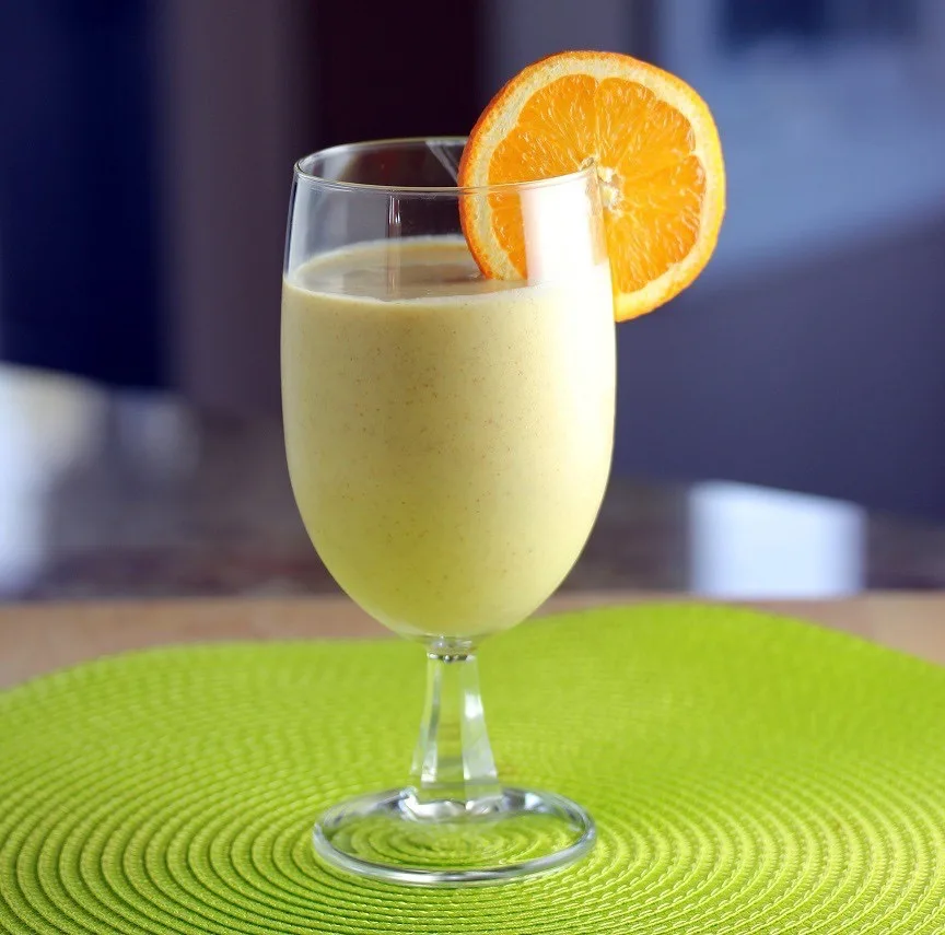 A tropical sunshine smoothie served in a stemmed glass and garnished with an orange slice