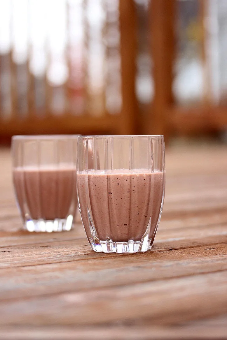 two glasses with a raspberry and yogurt smoothie shown outside on a deck