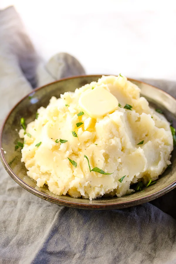 Finished mashed potatoes in a serving bowl topped with a pat of butter