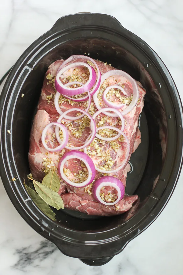 Pork butt in the slow cooker topped with sliced red onion before cooking