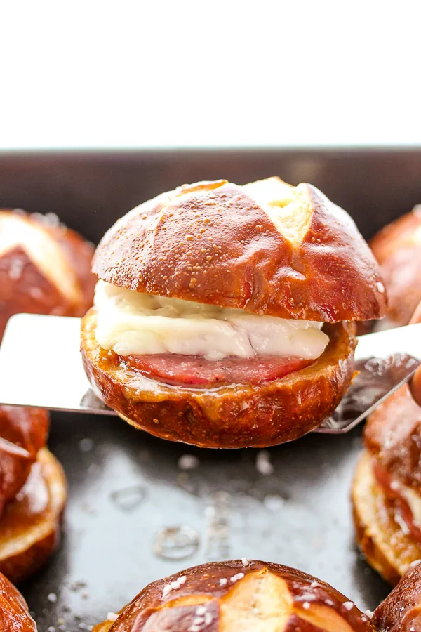 Close up showing cooked pretzel bun slider on a spatula to be removed from the baking dish.