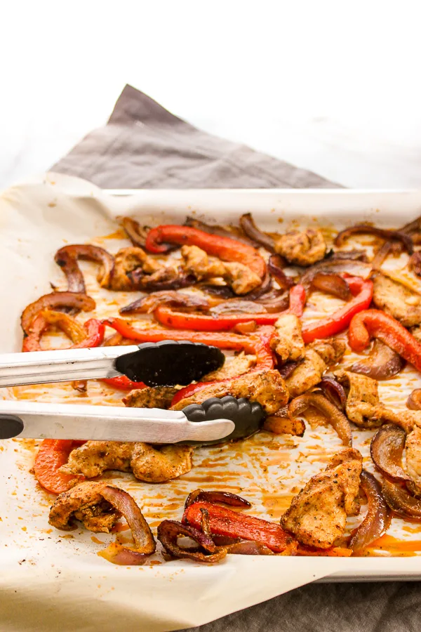 roasted chicken, pepper and onions on a sheet pan lined with parchment paper