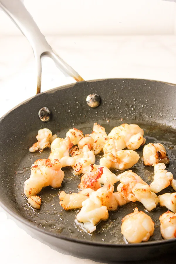 Chunks of lobster meat sautéing in a skillet.