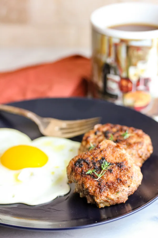 Close up of two cooked sausages garnished with fresh thyme and plated with a sunny side egg.