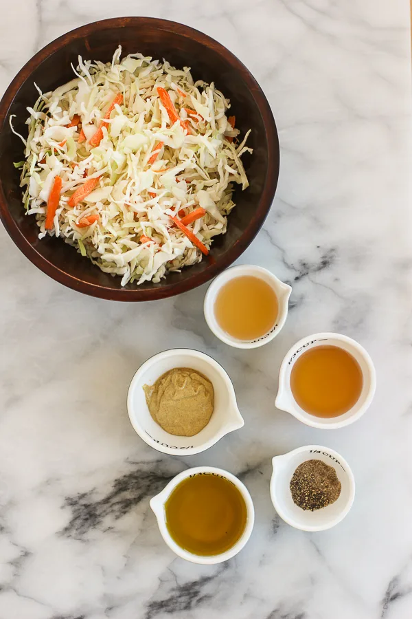 Coleslaw mix in a bowl along with the ingredients needed for the dressing in small bowls