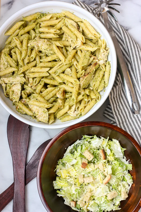 Grilled Chicken Pesto Pasta in a serving bowl along with a caesar salad in a serving bowl