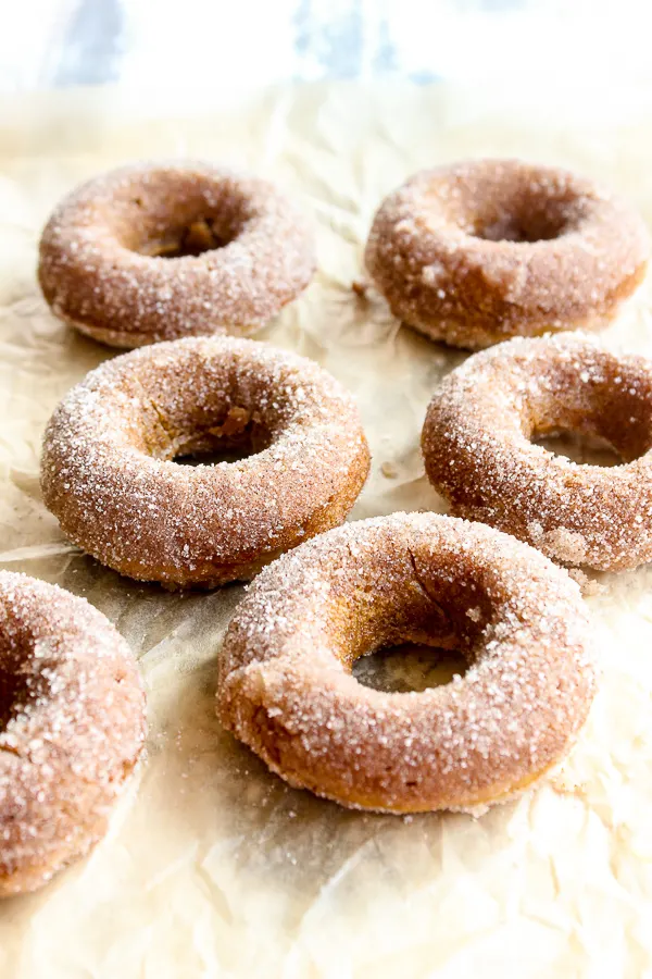 Baked Pumpkin Spiced Donuts on parchment paper after baking and dipping in sugar mixture