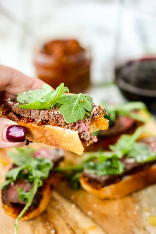 Sun-Dried Tomato Pesto Beef Crostini being held with a bite taken out of it