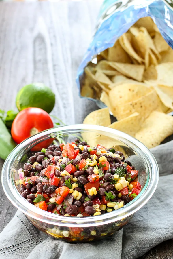 Cowboy Caviar Dip served with tortilla chips with tomato and lime in the background