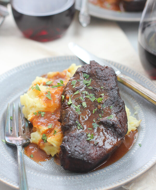 Shot of plated short ribs, mashed potatoes and sauce served with red wine