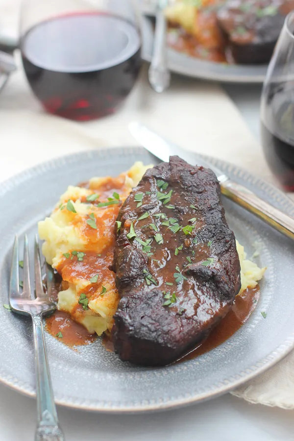 Shot of plated short ribs, mashed potatoes and sauce served with red wine