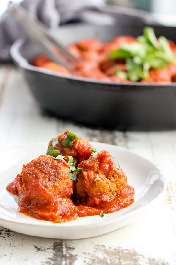 Plated meatballs in the forefront and cast iron skillet with meatballs in the background