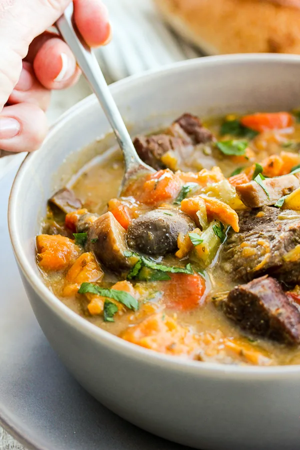 Instant Pot Sweet Potato Mushroom Beef Stew on a spoon over the bowl.