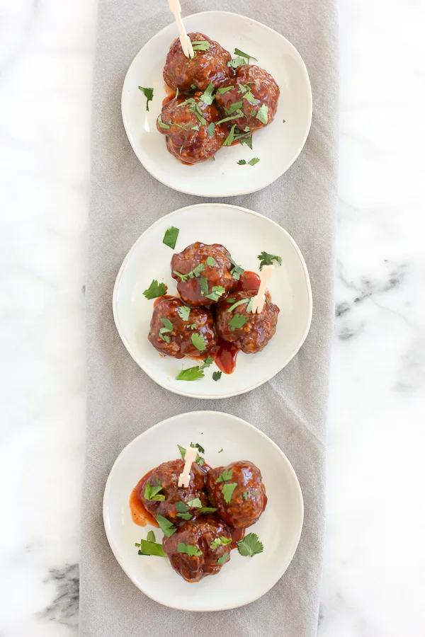 Baked meatballs coated with BBQ sauce and plated on 3 small plates.