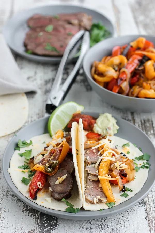 Cooked steak and pepper on a plate and in a bowl and plated fajitas on tortillas