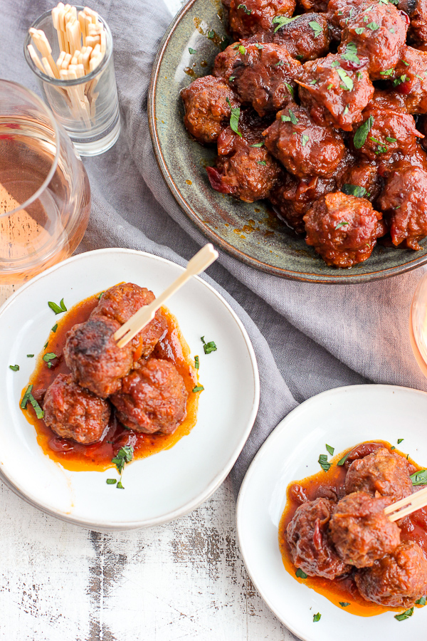 Meatballs plated with cocktail toothpicks along with a glass of wine and meatballs in a serving dish