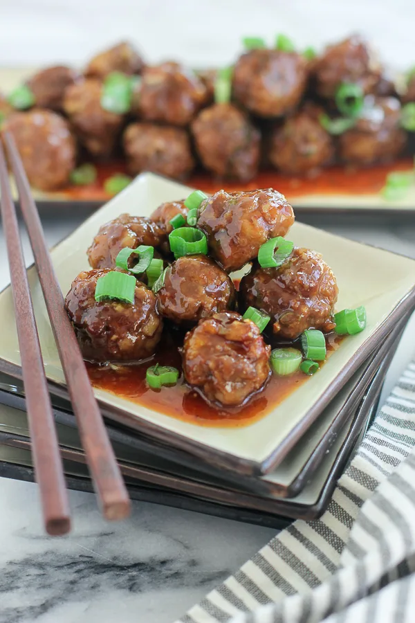 Meatballs plated with chop sticks with platter of meatball in the background
