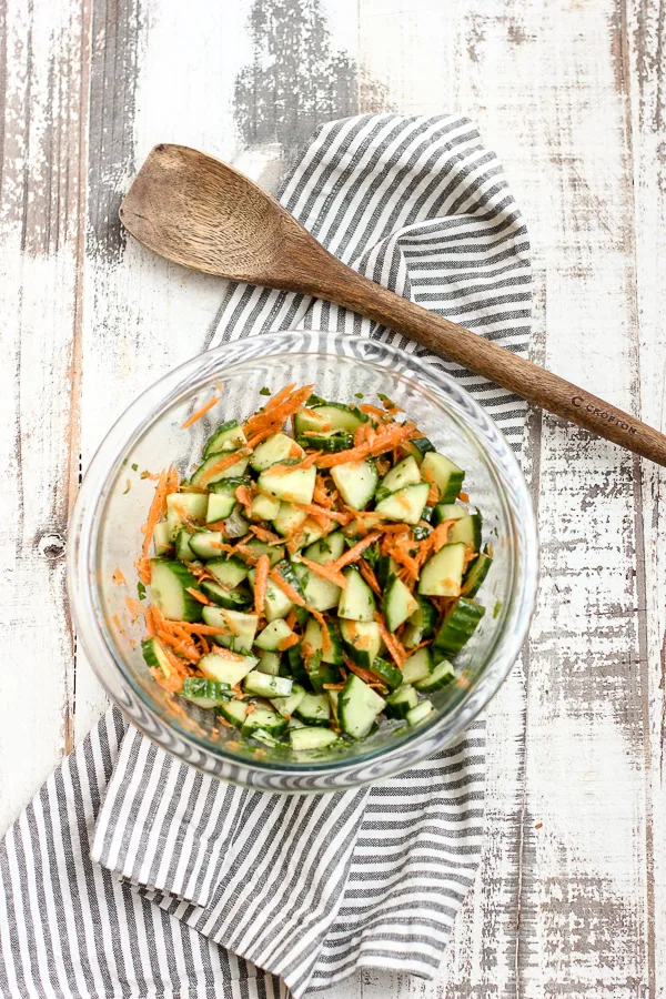 Finished Asian style cucumber salad in the mixing bowl with th wooden spoon next to it