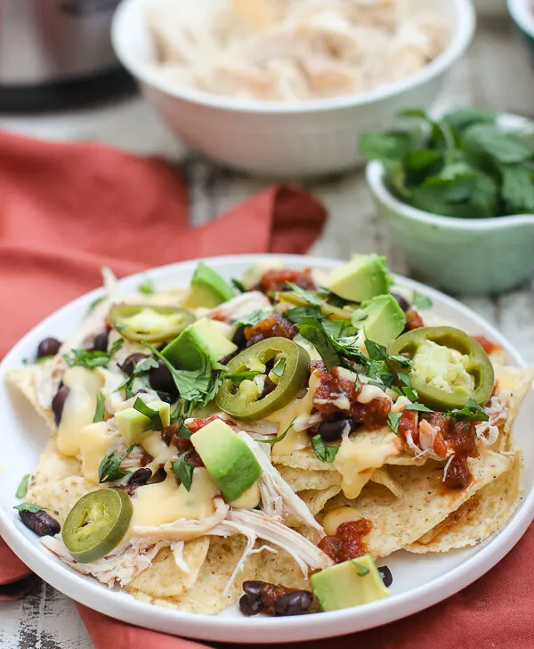 A plate of nachos made up with the toppings in the background