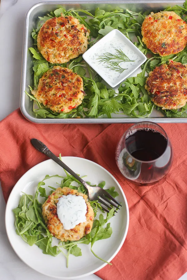 overhead picture of crab cake on plate and tray of crab cakes