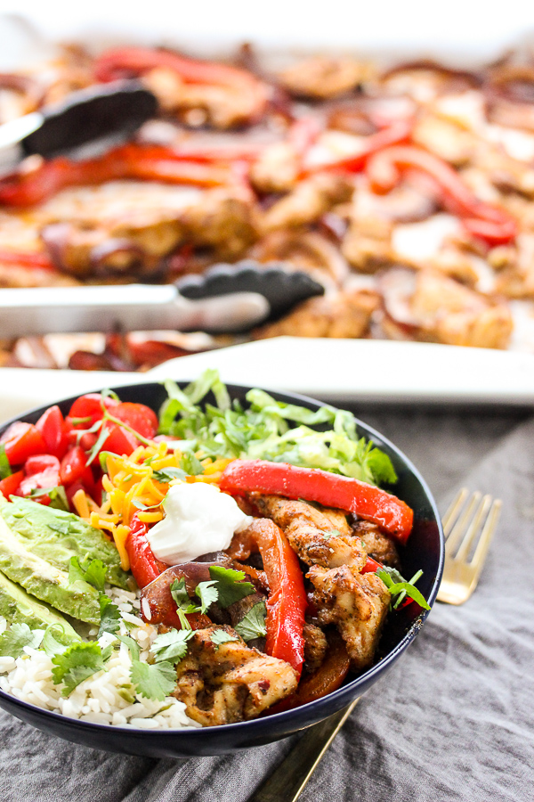 Close up shot of bowl of chicken fajitas with sheet pan of chicken fajitas in background