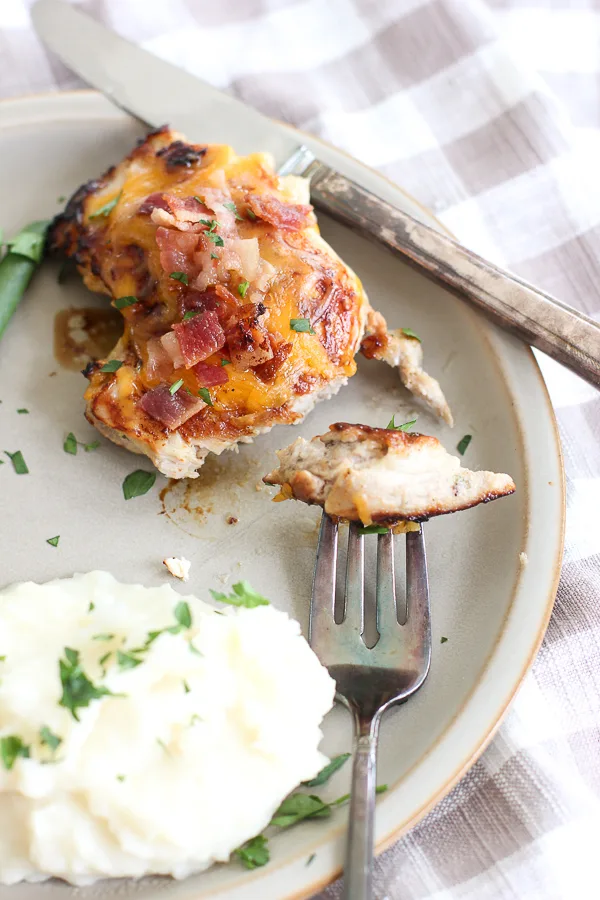 Cheddar cheese chicken thigh with bacon on the plate with a cut piece on a fork.