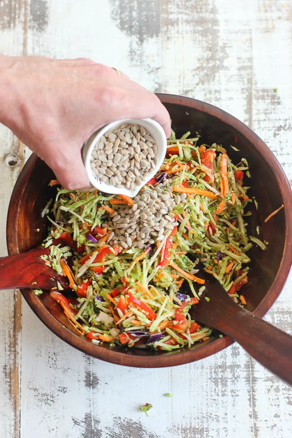 Adding the sunflower seeds after tossing the salad with the dressing.