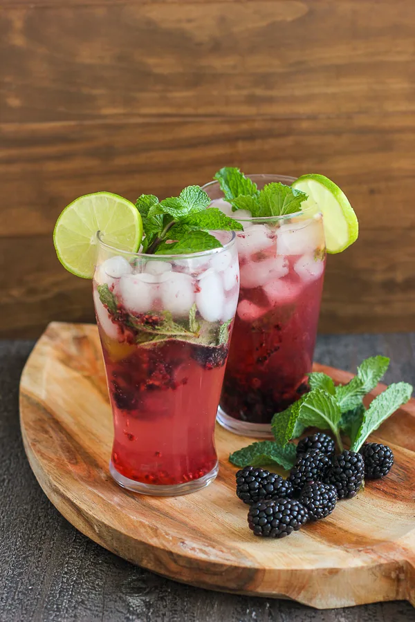 Two Blackberry Mint Sparkler Mocktails garnished with fresh lime and Fresh mint on a serving tray.