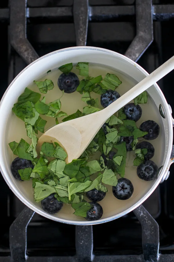 Blueberries and basil in a saucepan in process of making the blueberry simple syrup