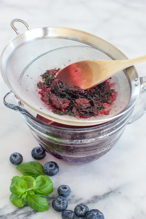 Straining the the blueberry basil simple syrup through a fine mesh strainer into a bowl