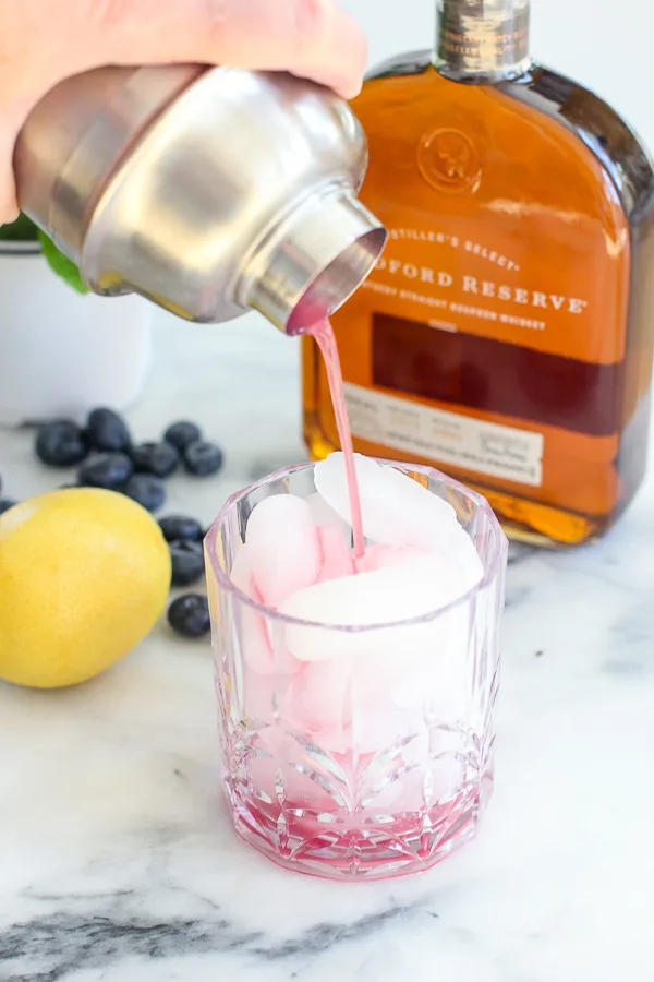 Pouring the cocktail out of the cocktail shaker into a rocks glass filled with ice