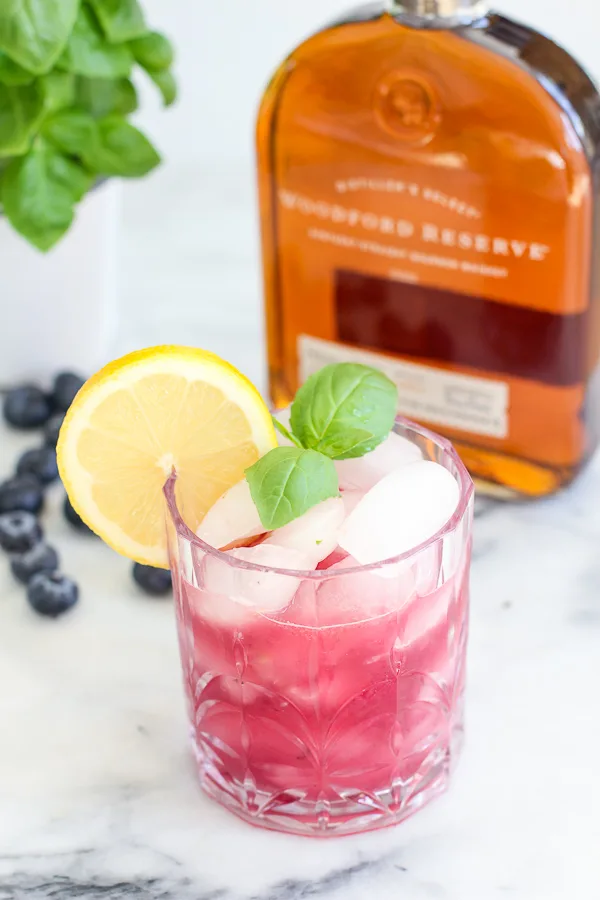 Finished blueberry basil bourbon smash in a cocktail glass garnished with a lemon slice and fresh basil