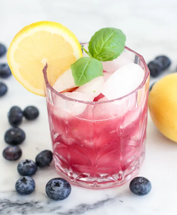 blueberry basil bourbon smash served in a rocks glass garnished with fresh lemon and basil