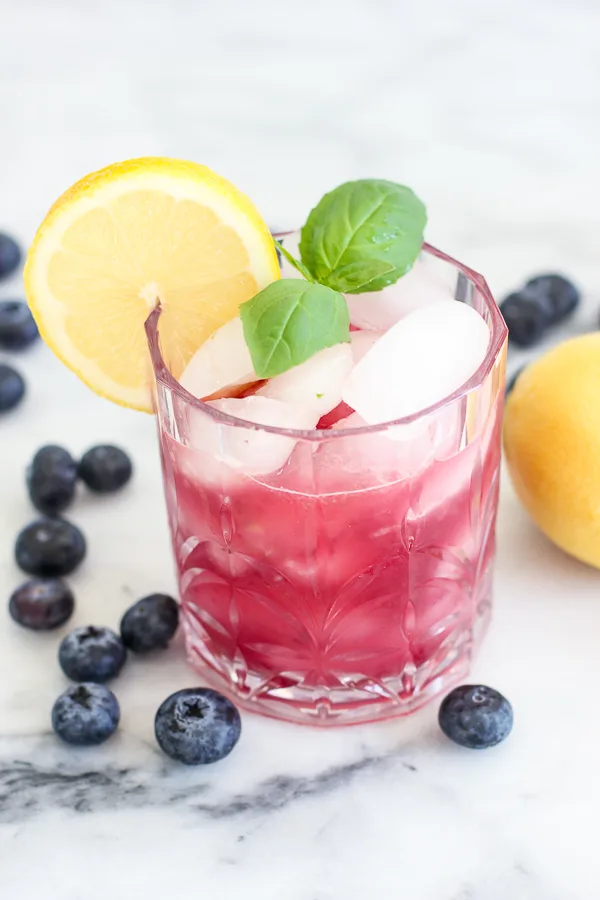 blueberry basil bourbon smash served in a rocks glass garnished with fresh lemon and basil