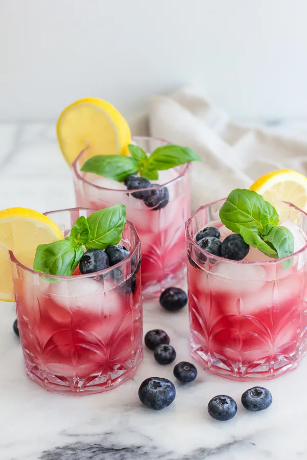 Three blueberry basil bourbon smash cocktails shown together with garnishes