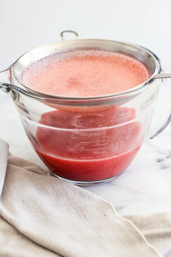 Straining pureed strawberries into a medium size bowl