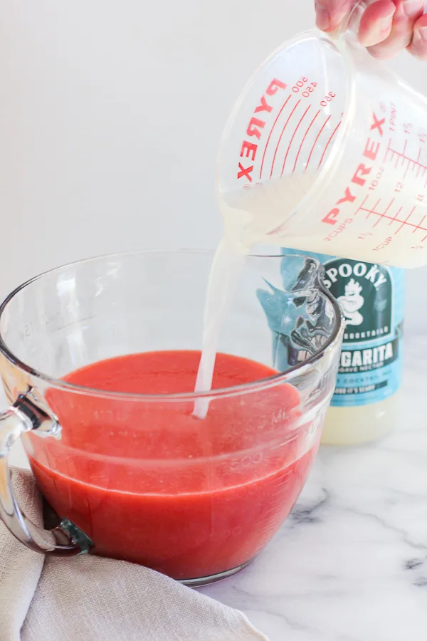 Pouring prepared margarita mix into medium size bowl containing pureed strawberries